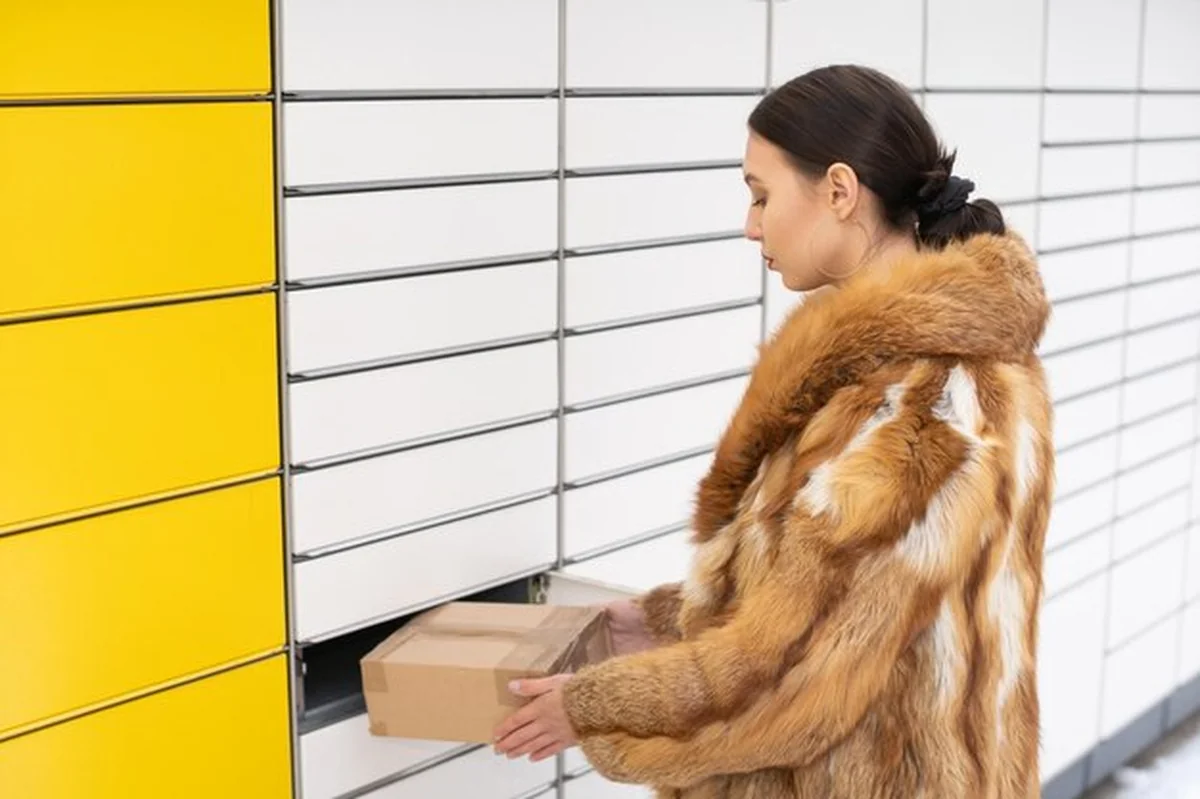 Kobieta w futrze podnosi paczkę z szafki do przesyłek